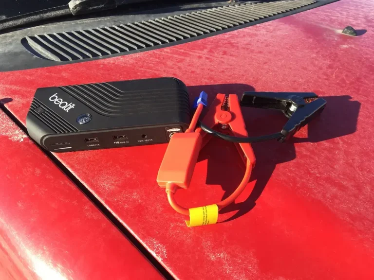 Driver uses a portable jump starter beside a sedan with the hood open on a quiet roadside.