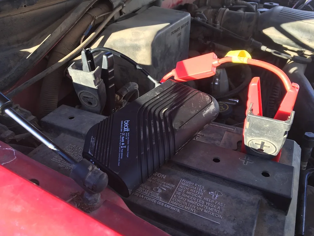 Close-up of a heavy-duty booster pack connected to a truck battery with thick jumper cables.