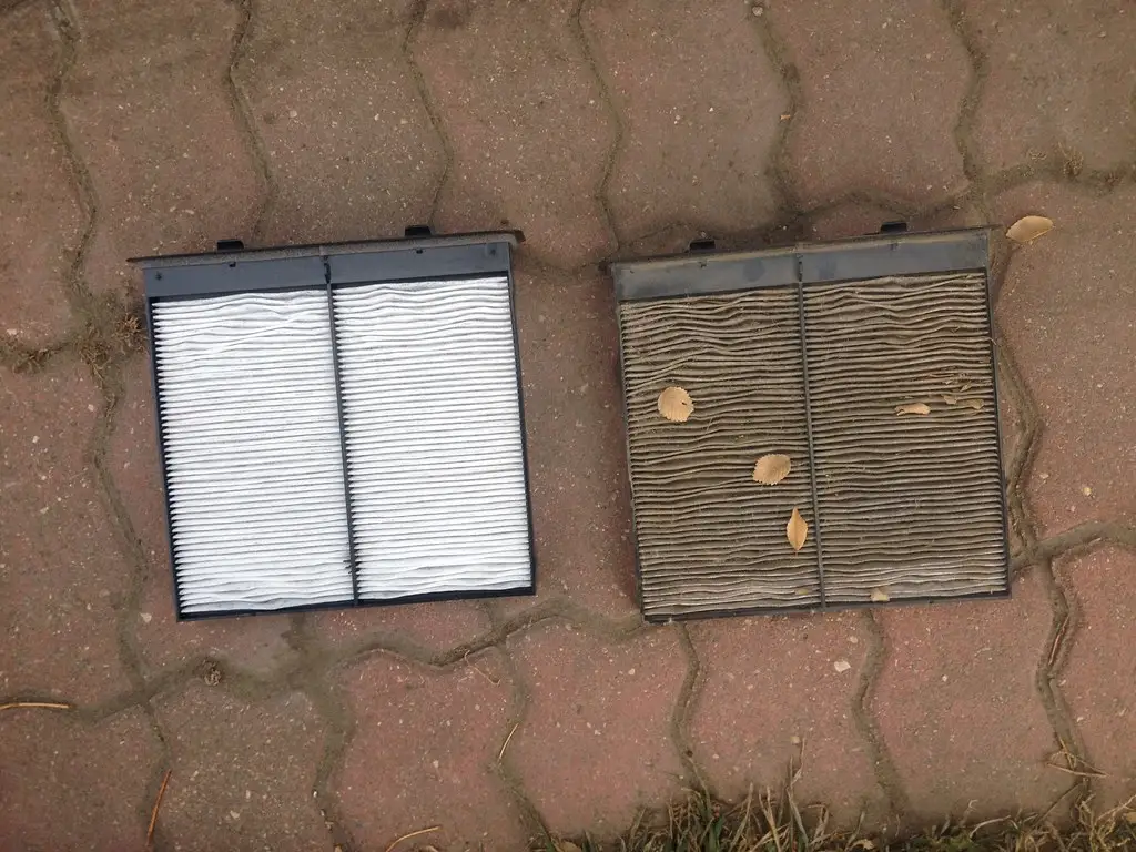 Car owner holds a K&N cabin air filter beside an open glove box in a garage