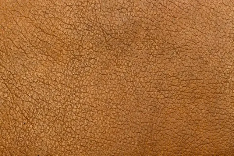 Person wiping a beige leather car seat with cleaner and microfiber cloth in natural light