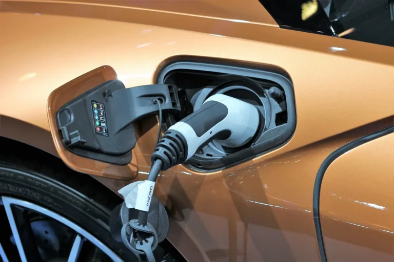 Person checking an electric car battery status on a smartphone beside a parked EV