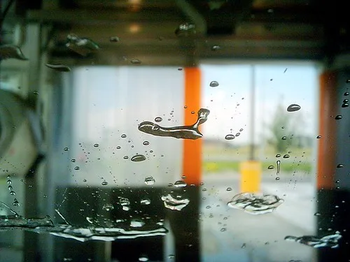 A microfiber mitt washing a car hood with soap and water droplets