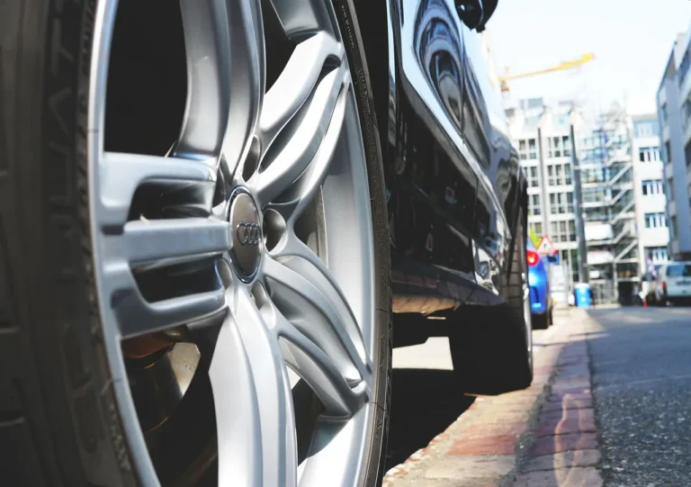 A black sedan with one freshly glossy tire and another matte tire in a sunny driveway.