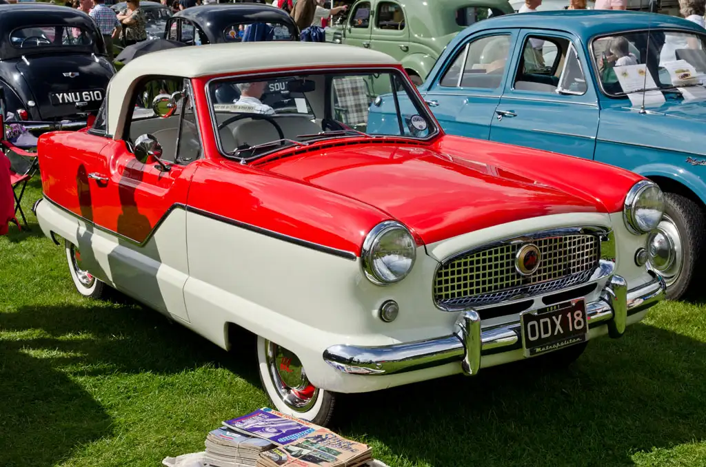 Hands tuning a vintage car radio on a classic dashboard with worn chrome knobs.