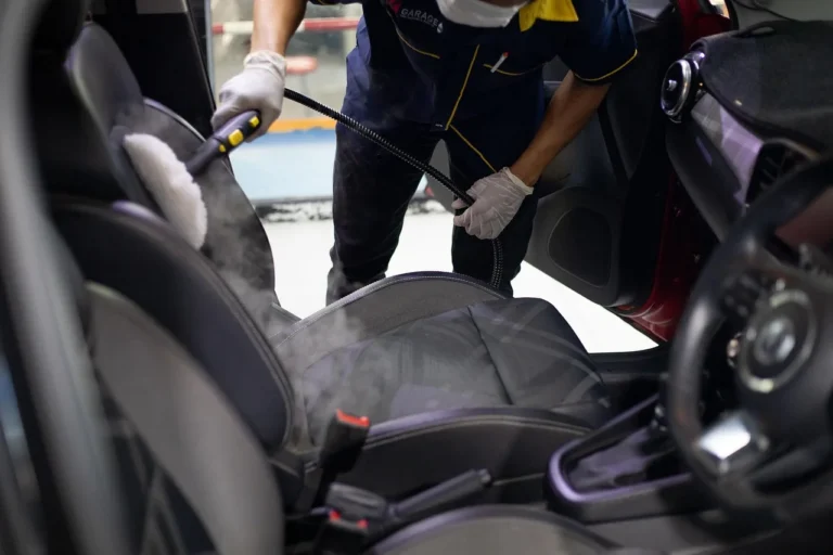 Portable steam cleaner beside an open car, with hose, nozzle, and cleaned seat visible
