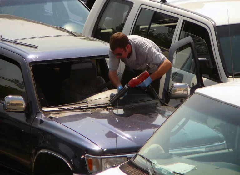 Auto glass repair technician working on a car windshield in a driveway with the customer nearby
