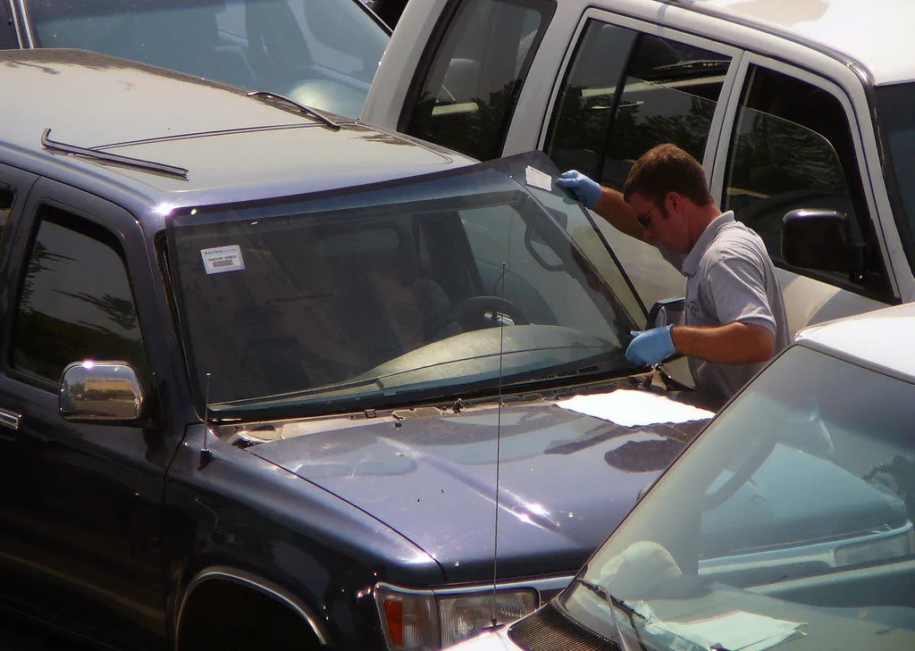 Hands using a suction cup and sealant gun on a cracked windshield during auto glass repair