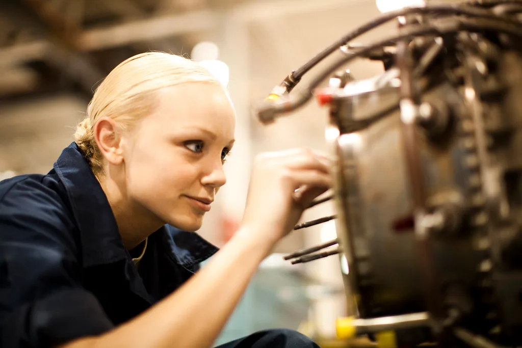 Hands measure cylinder head and gasket surfaces on an engine bench.