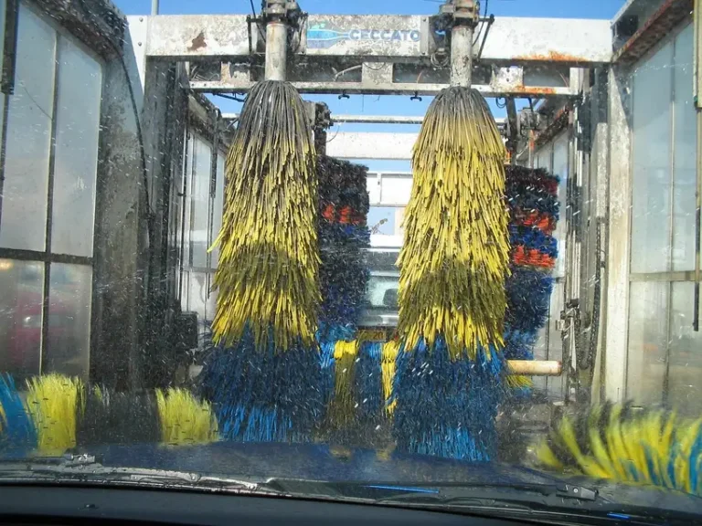 Touchless and brush car wash methods cleaning a silver sedan in a bright wash bay