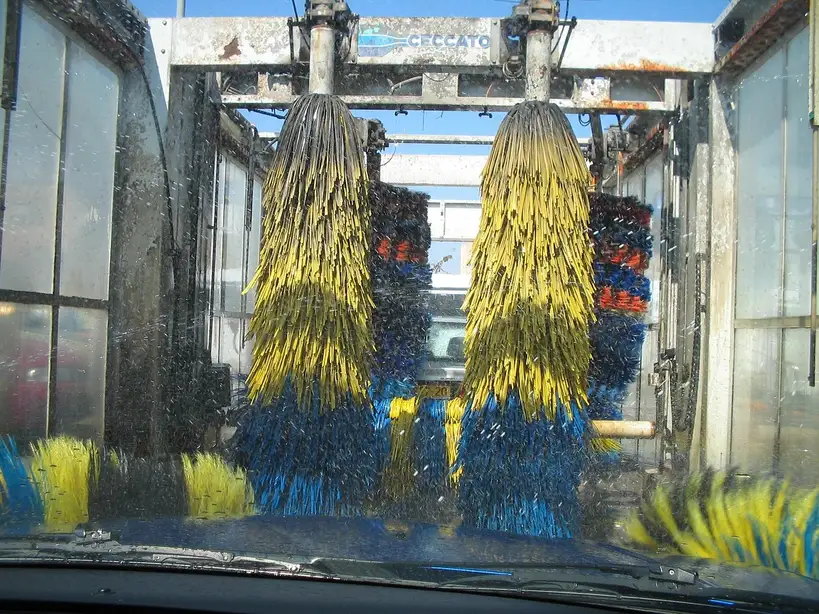 Touchless and brush car wash methods cleaning a silver sedan in a bright wash bay