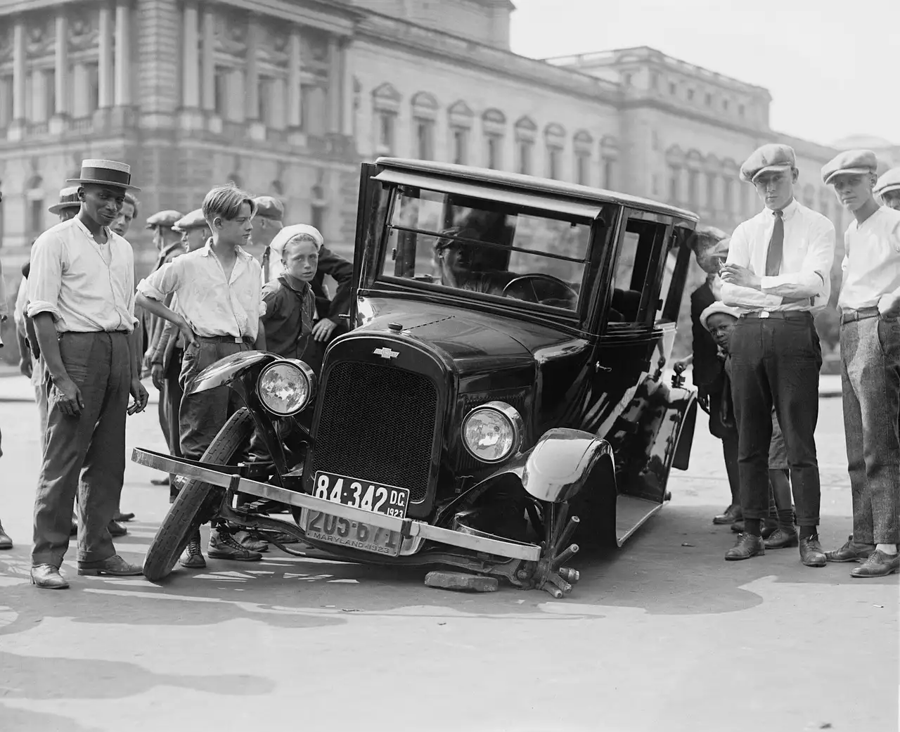 Damaged sedan on a dealership lot with a dealer inspecting the body damage and clipboard