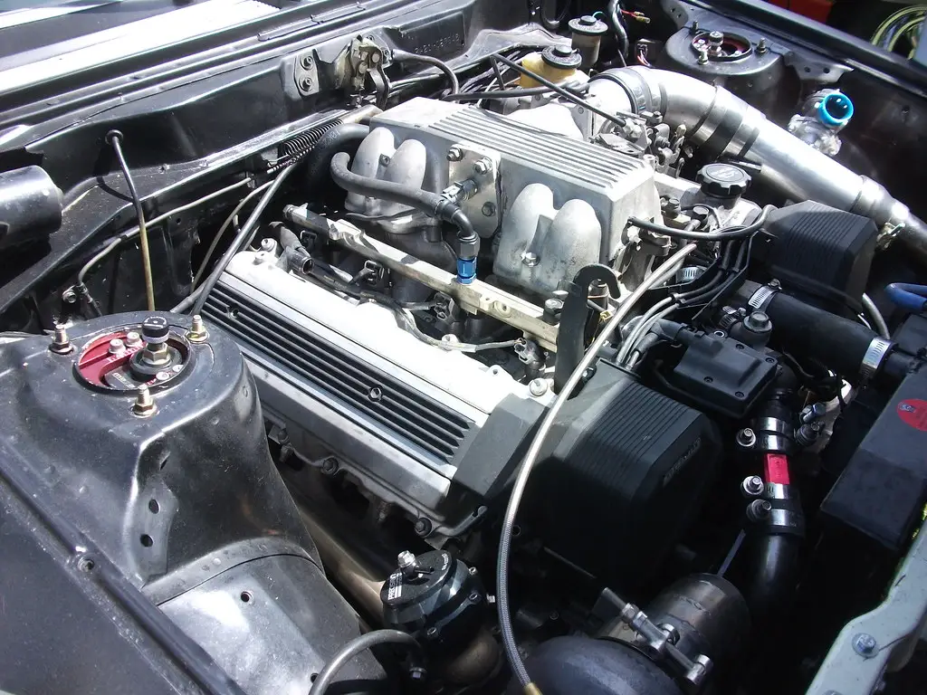 Close-up of a V8 engine bay with a mechanic pointing at the intake manifold.