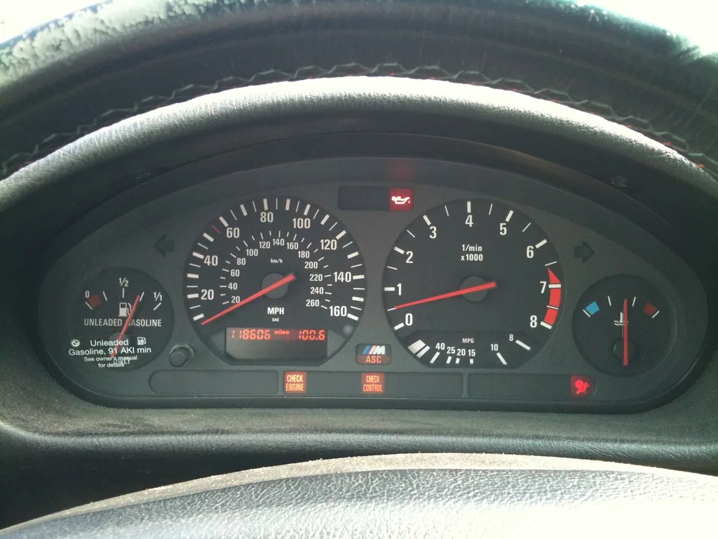 Mechanic uses a scanner under a BMW dashboard to read a warning code.