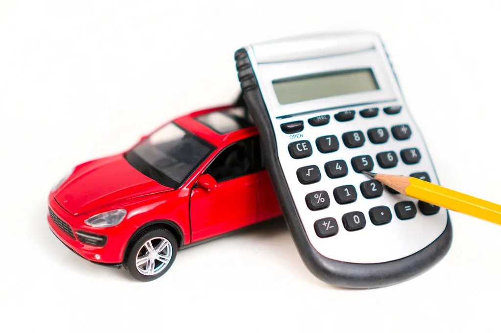 Hand using a calculator beside a car repair estimate and emergency savings envelope