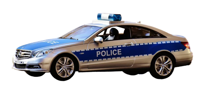 Police officer tapping a sedan trunk during a roadside stop at dusk