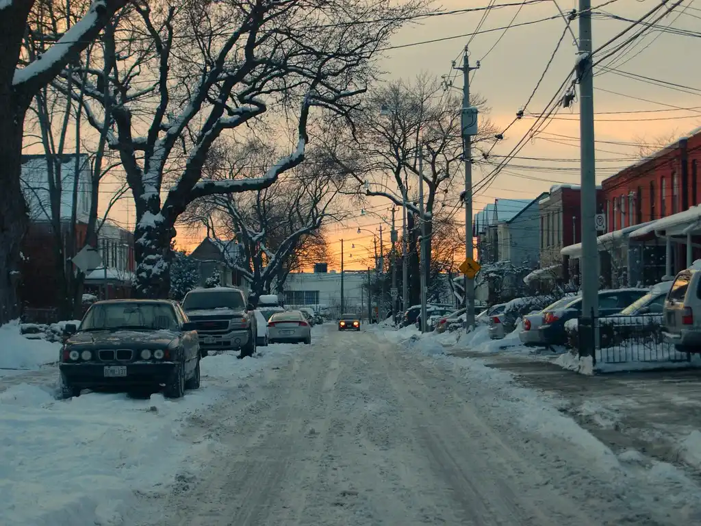 Winter driveway scene showing a car with a windshield cover beside a folded full car cover